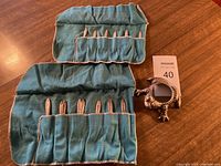 Two cloth rolls containing spoons and a metal frog magnifier on wooden surface