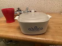 Vintage Corning Ware white casserole with blue floral pattern and glass lid on wooden table surface