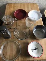 Photo shows assortment of bowls, mixing bowls, coffee pot, electric can opener, and baking dishes arranged on wooden surface.