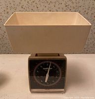White plastic platform kitchen scale with black dial face showing pounds and ounces.