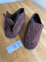 Pair of men's brown wide slippers size 11 with ribbed fabric and Velcro closure shown from top and side angle on wooden table.