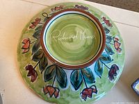 Green Richard Mund pottery plate with floral design and signature visible