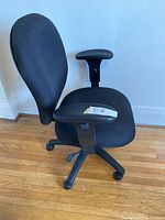 Side view of black adjustable office chair with padded fabric seat and backrest, adjustable armrest, and five-wheel base on wood floor.