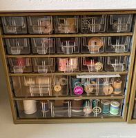 Front view of clear plastic organizer with multiple small drawers containing various wooden bobbins and sewing threads