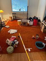 Wide angle view of the full carpet laid out in an empty room with some scattered items and measuring tape showing size.