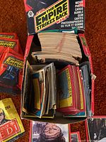 Opened display box showing a large collection of Empire Strikes Back trading cards inside, along with loose cards and one unopened Return of the Jedi pack.