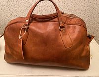 Photo of vintage brown leather duffel bag in weathered condition with sturdy handles and zipper showing tear but functional