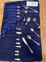 Full lot of assorted silver spoons, forks, and serving tools neatly arranged in blue roll-up cloth cases showing a variety of small utensils and flatware.