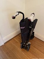 Folded black Airgo transport wheelchair with white handles against wall