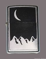 Front view showing crescent moon and mountain design on textured black background of the silver-tone Zippo lighter.