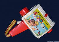 Side view of the Fisher-Price toy camera showing white body and large red lens dial with color filter options graphics and picture disc storage area with stickers of children and birds.