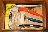 Photo showing five vintage large fishing lures in a box highlighting colors and shapes