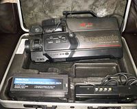 Panasonic OmniMovie AF X8 VHS camcorder in hard plastic case with two rechargeable battery packs and battery charger inside the case compartments.