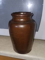 Front view of brown glazed crock showing rounded shoulder and narrow neck with flared rim.