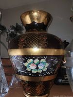 Front view of large vase showing deep purple color, wide gold trim, hand painted flowers, and ruby red bead decoration.