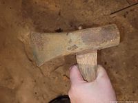 Rusty axe head with wedge shape held in hand, showing significant surface rust and patina.