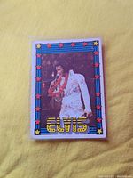 Front view of vintage Elvis Presley trading card in plastic sleeve, showing Elvis in white jumpsuit with red and blue star border and 'ELVIS' text at bottom.