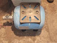 Top view of blue cylindrical water pressure tank with black mounting bracket and pipe connection fitting.