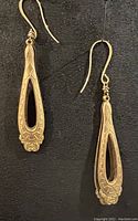 Pair of antique brass patterned drop earrings on gold plated ear wires shown against a dark background.
