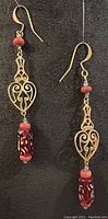 Pair of antique brass earrings with heart-shaped design and red-gold glass beads on black background.