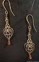 Full view of both antique brass heart-shaped earrings with gold plated ear wires and fire orange crystals.