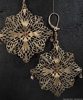 Pair of antique brass filigree snowflake earrings with gold plated ear wires and Swarovski crystal accents shown against black background