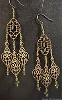 Pair of brass chandelier earrings displayed on black fabric showing full length and detailing of design and wire wrapping.