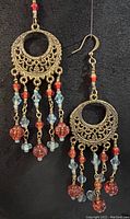 Full view of one brass chandelier earring hanging, showing its length and bead details.