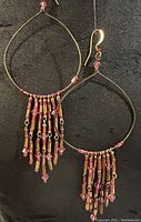 Full view of both gold plated hoop earrings showing teardrop shape and pink and gold glass bead tassels with Swarovski crystals.