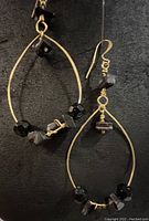 Front view of one gold plated brass hoop earring with faceted black crystal and black agate beads, hanging on gold plated ear wire.