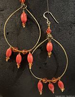 Pair of gold plated brass teardrop-shaped hoop earrings with red wood, glass, and Swarovski crystal beads set against a black background.