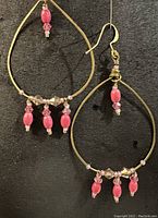 Pair of gold plated brass hoop earrings on black background. Earrings have gold plated ear wires and pink wood, glass and gold Swarovski crystal accents hanging from the hoops.