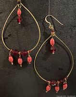 Pair of gold plated brass teardrop hoop earrings on black background showing red wood, red glass, and Swarovski crystal beads along the bottom and top wire wrapping detail.