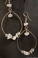 Full view of pair of gold plated brass oval hoop earrings with white agate and clear Swarovski crystal accents on black background
