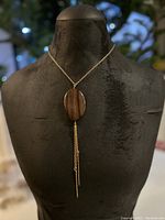 Full view of gold plated chain necklace with oval wood pendant and hanging gold chains.