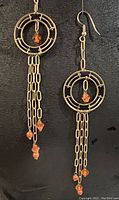 Pair of long gold plated brass tassel earrings displayed on black background.