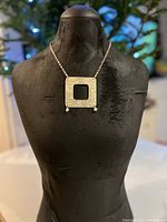 Front view of the silver plated brass necklace displayed on a black mannequin showing the square pendant and chain.