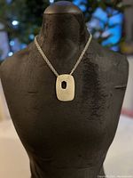 Silver plated brass necklace displayed on black stand, showing full necklace length and pendant placement.