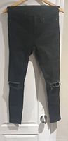 Black skinny leg jeans with ripped knees hanging on a wooden hanger.