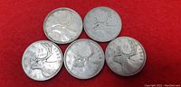 Five Canadian quarters showing reverse sides featuring caribou designs on a red background.