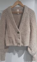 Front view of the beige wool and alpaca blend cardigan hanging on a wooden hanger, showing button detail and knit texture.