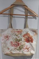 Front view of quilted tote bag with large floral print in shades of orange, pink, and green on cream fabric, hanging on wooden hanger.