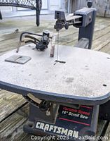 Close-up of Craftsman 16 inch scroll saw on wooden surface, showing adjustable blade holder, tension spring, and metal work surface with wear.