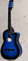 Front view of blue electric/acoustic guitar without strings, showing body, neck, fretboard, and tuning pegs.