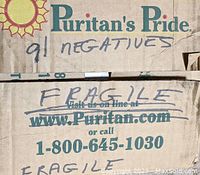 Photo of the top of a cardboard box labeled "Puritan's Pride" with handwritten notes "91 negatives" and "Fragile" on it.