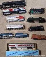 Full view of all train engines and car on a beige carpet, showing variety of locomotives, tender, and boxed passenger car.