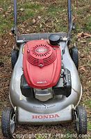 Photo of a silver Honda lawnmower with a red engine cover, four wheels (larger rear wheels) on grass surface.