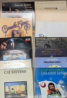 Photo showing a collection of 11 vinyl records from popular folk artists including Simon & Garfunkel, Paul Simon, Harry Chapin, Joni Mitchell, Carole King, Don McLean, Neil Young, and Cat Stevens.