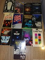 Photo of 13 assorted paperback books laid out on a carpeted floor, titles visible