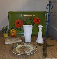 Photo showing a green metal bread box with floral designs and various small kitchen decorative items on a wooden surface.